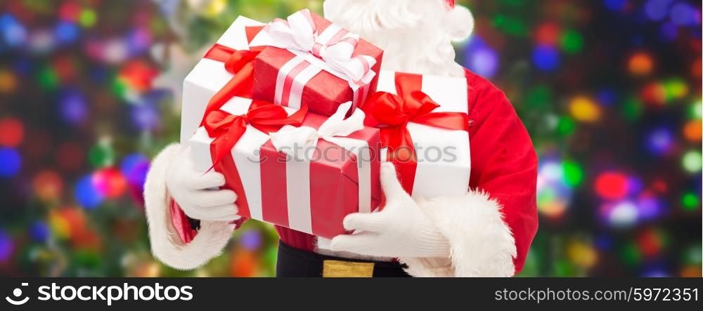 christmas, holidays and people concept - close up of santa claus with gift boxes over lights background