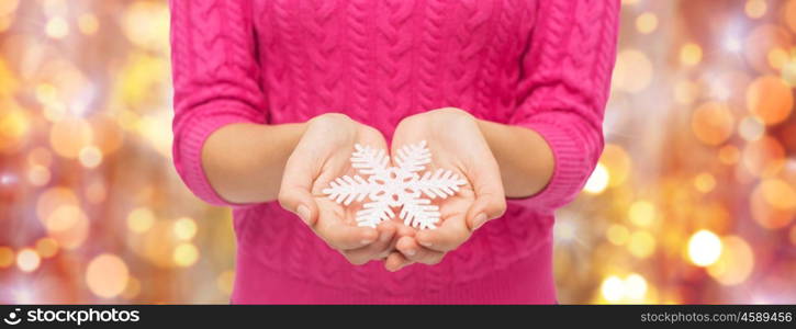 christmas, holidays and people concept - close up of woman in pink sweater holding snowflake over lights background