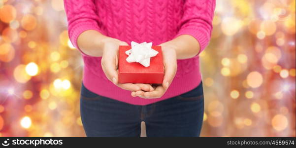 christmas, holidays and people concept - close up of woman in pink sweater holding gift box over lights background