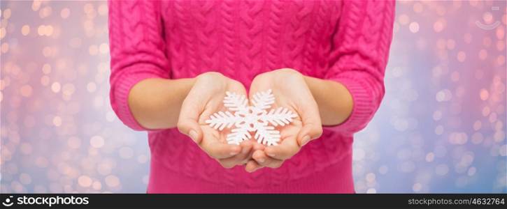 christmas, holidays and people concept - close up of woman in pink sweater holding snowflake over rose quartz and serenity lights background