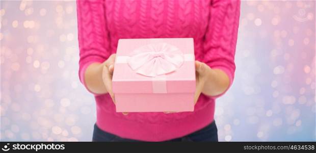 christmas, holidays and people concept - close up of woman in pink sweater holding gift box over rose quartz and serenity lights background