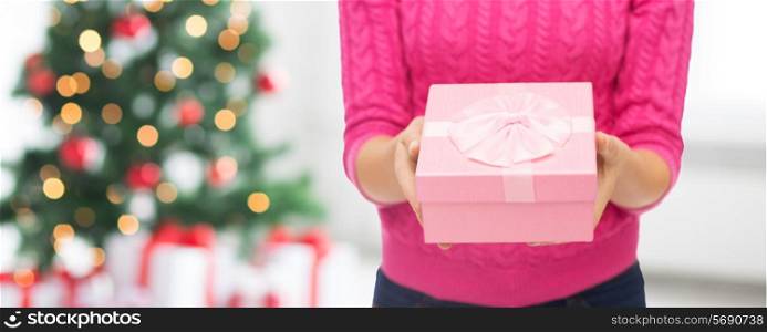 christmas, holidays and people concept - close up of woman in pink sweater holding gift box over living room and tree background
