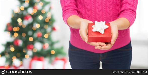 christmas, holidays and people concept - close up of woman in pink sweater holding gift box over living room and tree background