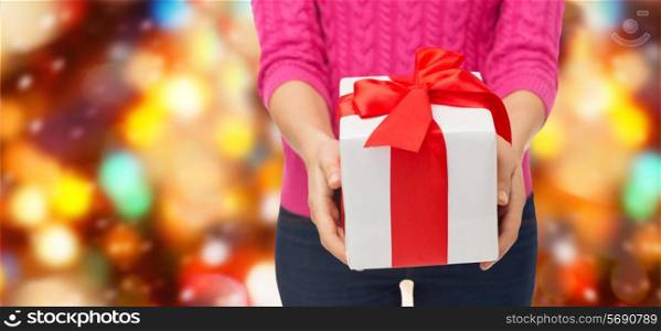 christmas, holidays and people concept - close up of woman in pink sweater holding gift box over red lights background