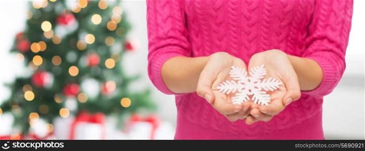 christmas, holidays and people concept - close up of woman in pink sweater holding snowflake over living room and tree background