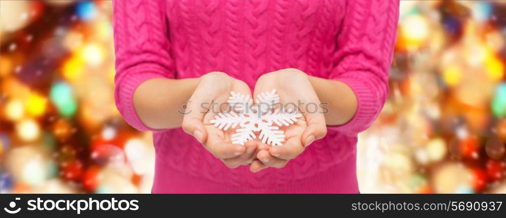 christmas, holidays and people concept - close up of woman in pink sweater holding snowflake over red lights background