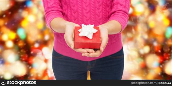 christmas, holidays and people concept - close up of woman in pink sweater holding gift box over red lights background