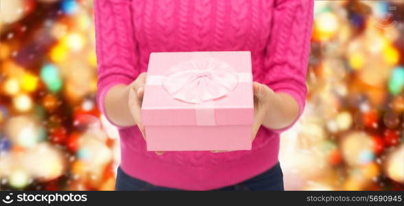 christmas, holidays and people concept - close up of woman in pink sweater holding gift box over red lights background