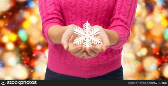 christmas, holidays and people concept - close up of woman in pink sweater holding snowflake decoration over red lights background