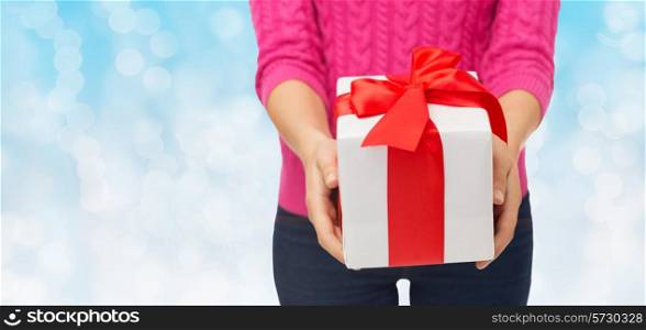 christmas, holidays and people concept - close up of woman in pink sweater holding gift box over blue lights background