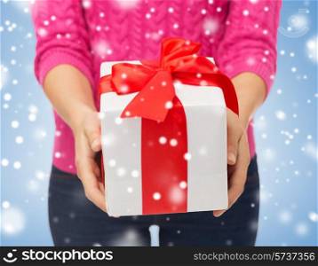 christmas, holidays and people concept - close up of woman in pink sweater holding gift box over blue background with snow over blue background with snow