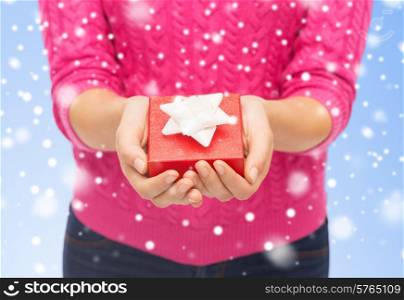 christmas, holidays and people concept - close up of woman in pink sweater holding small red gift box over blue background with snow over blue background with snow