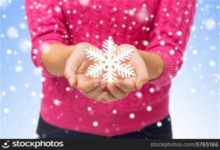 christmas, holidays and people concept - close up of woman in pink sweater holding snowflake decoration over blue background with snow