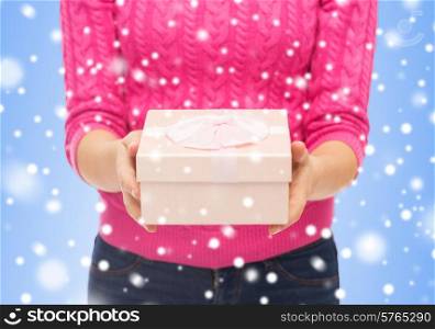christmas, holidays and people concept - close up of woman in pink sweater holding gift box over blue background with snowover blue background with snow