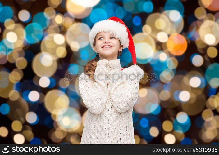 christmas, holidays and people concept - dreaming girl in santa helper hat over lights background. dreaming girl in santa helper hat over lights