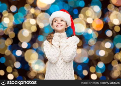 christmas, holidays and people concept - dreaming girl in santa helper hat over lights background. dreaming girl in santa helper hat over lights