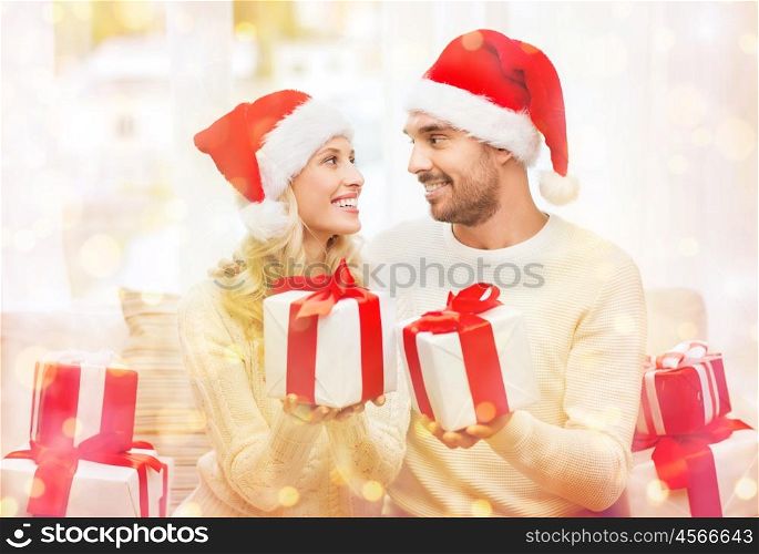 christmas, holidays and people concept - happy couple in santa hats exchanging gifts at home over lights