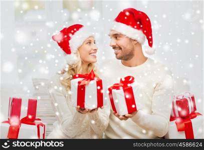 christmas, holidays and people concept - happy couple in santa hats exchanging gifts at home