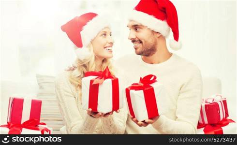 christmas, holidays and people concept - happy couple in santa hats exchanging gifts at home. happy couple at home exchanging christmas gifts