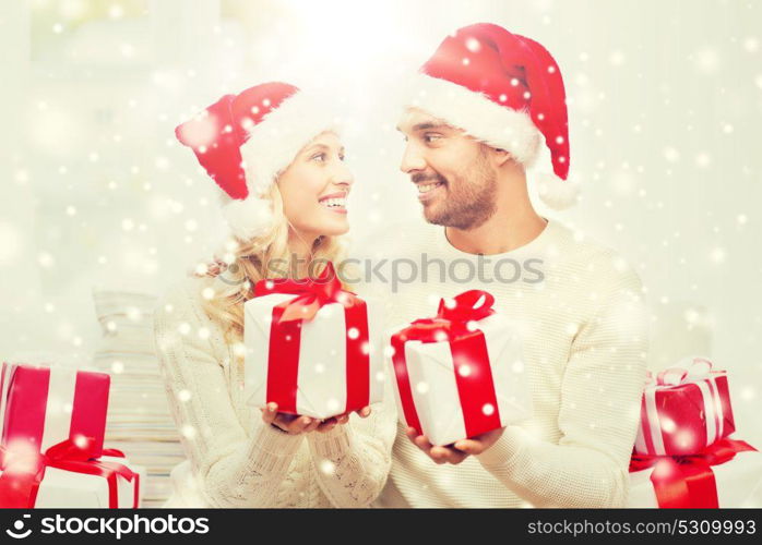 christmas, holidays and people concept - happy couple in santa hats exchanging gifts at home. happy couple at home exchanging christmas gifts