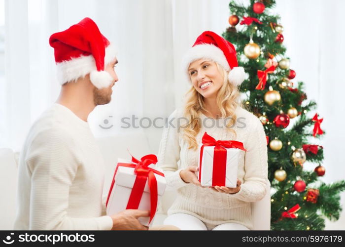 christmas, holidays and people concept - happy couple in santa hats exchanging gifts at home