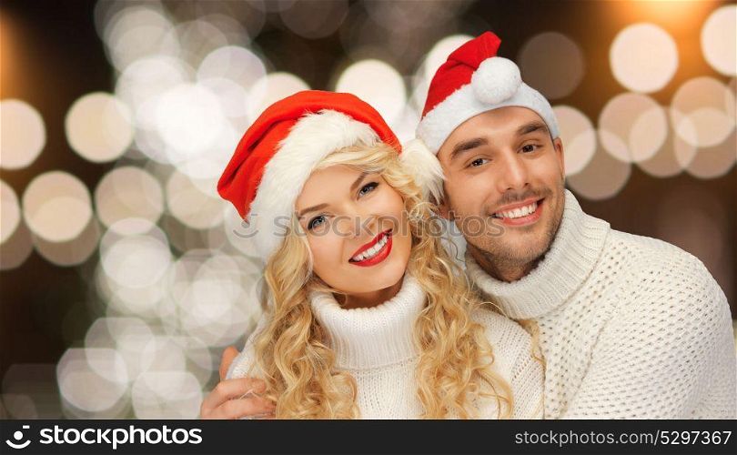 christmas, holidays and people concept - happy couple in santa hats over night lights background. happy couple in santa hats over christmas lights