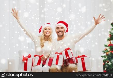christmas, holidays and people concept - happy couple in santa hats with gift boxes sitting on sofa at home