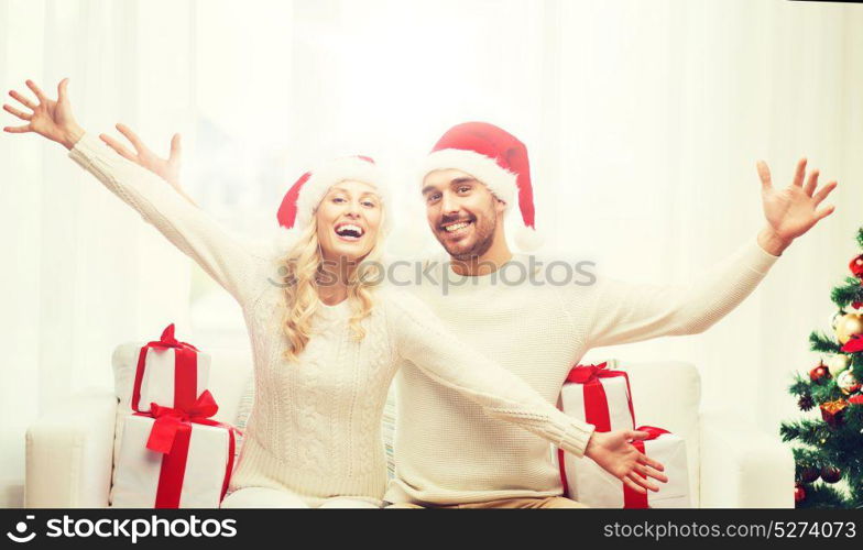 christmas, holidays and people concept - happy couple in santa hats with gift boxes sitting on sofa at home. happy couple at home with christmas gift boxes