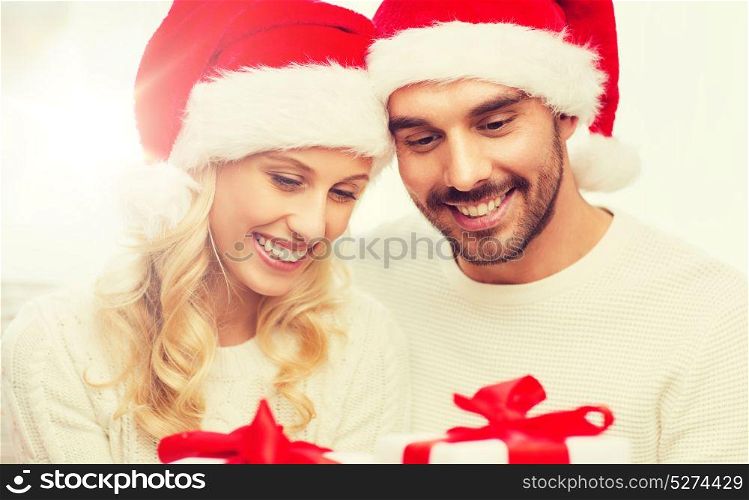 christmas, holidays and people concept - happy couple in santa hats with gift boxes sitting on sofa at home. happy couple at home with christmas gift boxes