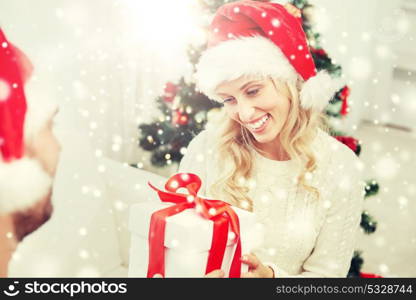 christmas, holidays and people concept - happy couple in santa hats with gift box sitting on sofa at home. happy couple at home with christmas gift box