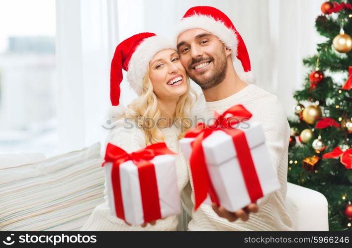 christmas, holidays and people concept - happy couple in santa hats with gift boxes sitting on sofa at home