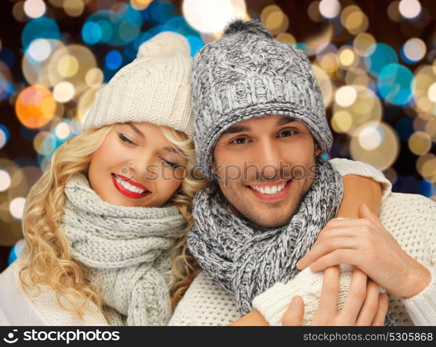 christmas, holidays and people concept - happy couple in winter hats over lights background. happy couple in hats over lights background