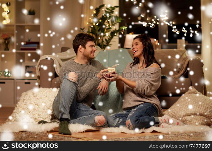 christmas, holidays and people concept - happy couple with gift box at home over snow. happy couple with gift box at home