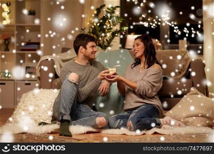 christmas, holidays and people concept - happy couple with gift box at home over snow. happy couple with gift box at home