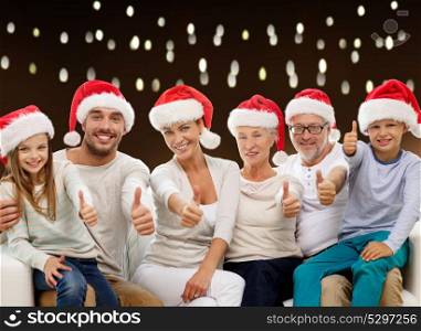 christmas, holidays and people concept - happy family in santa hats showing thumbs up gesture over lights background. family in christmas santa hats showing thumbs