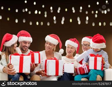 christmas, holidays and people concept - happy family in santa hats with gift boxes over lights background. happy family in santa hats with christmas gifts