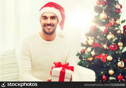 christmas, holidays and people concept - happy man in santa hat with gift box at home. happy man with christmas gift box at home