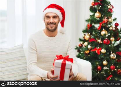 christmas, holidays and people concept - happy man in santa hat with gift box at home