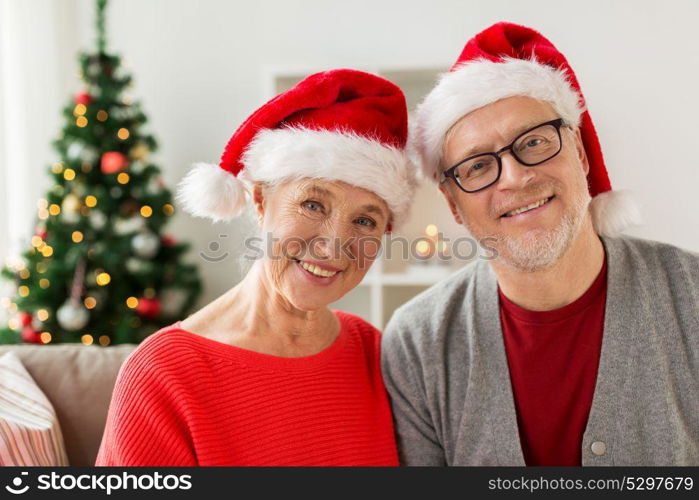 christmas, holidays and people concept - happy smiling senior couple in santa hats at home. happy senior couple in santa hats at christmas