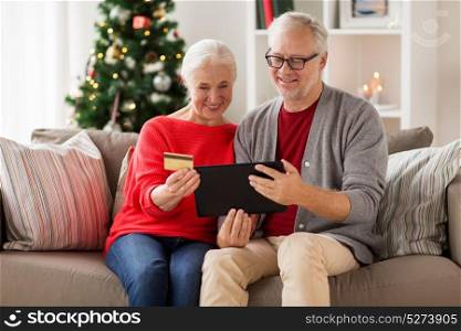 christmas, holidays and people concept - happy smiling senior couple with tablet pc computer and credit card shopping online at home. happy senior couple with tablet pc at christmas