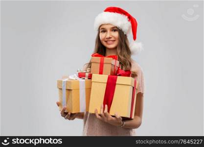christmas, holidays and people concept - happy smiling teenage girl in santa helper hat holding gift box over grey background. teenage girl in santa hat with christmas gift