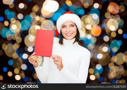 christmas, holidays and people concept - happy smiling woman in santa hat with greeting card over lights background. happy woman with christmas greeting card