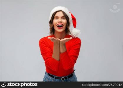 christmas, holidays and people concept - happy smiling young woman in santa helper hat sending air kiss over grey background. happy young woman in santa hat sending air kiss