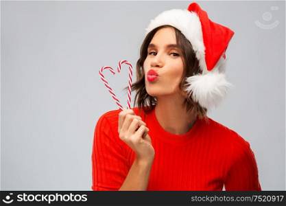christmas, holidays and people concept - happy smiling young woman in santa helper hat with candy canes making duck face over grey background. happy young woman in santa hat on christmas
