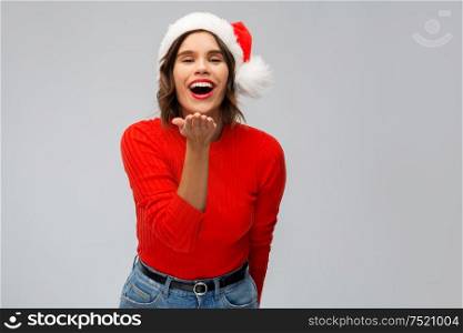 christmas, holidays and people concept - happy smiling young woman in santa helper hat sending air kiss over grey background. happy young woman in santa hat sending air kiss