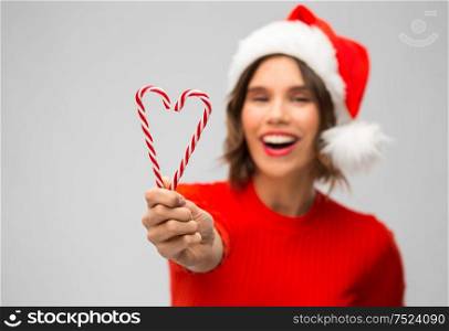 christmas holidays and people concept - happy smiling young woman in santa helper hat with candy canes over grey background. happy woman in santa hat showing candy canes