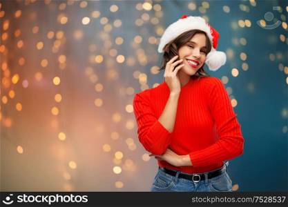 christmas, holidays and people concept - happy smiling young woman in santa helper hat over festive lights background. happy young woman in santa hat on christmas