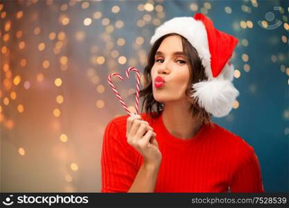 christmas, holidays and people concept - happy smiling young woman in santa helper hat with candy canes making duck face over festive lights background. happy young woman in santa hat on christmas
