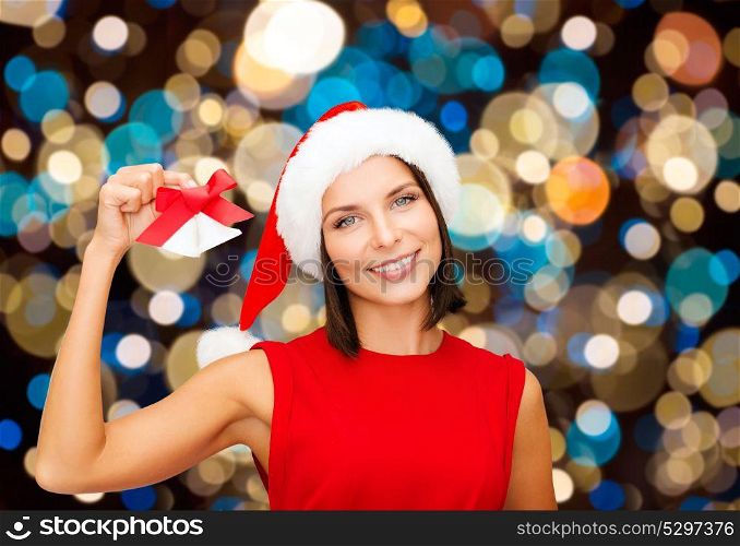 christmas, holidays and people concept - happy woman in santa hat with jingle bells over lights background. happy woman in santa hat with christmas bells