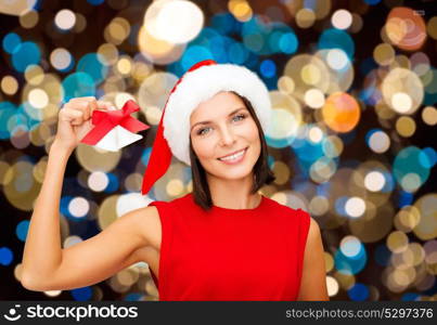 christmas, holidays and people concept - happy woman in santa hat with jingle bells over lights background. happy woman in santa hat with christmas bells